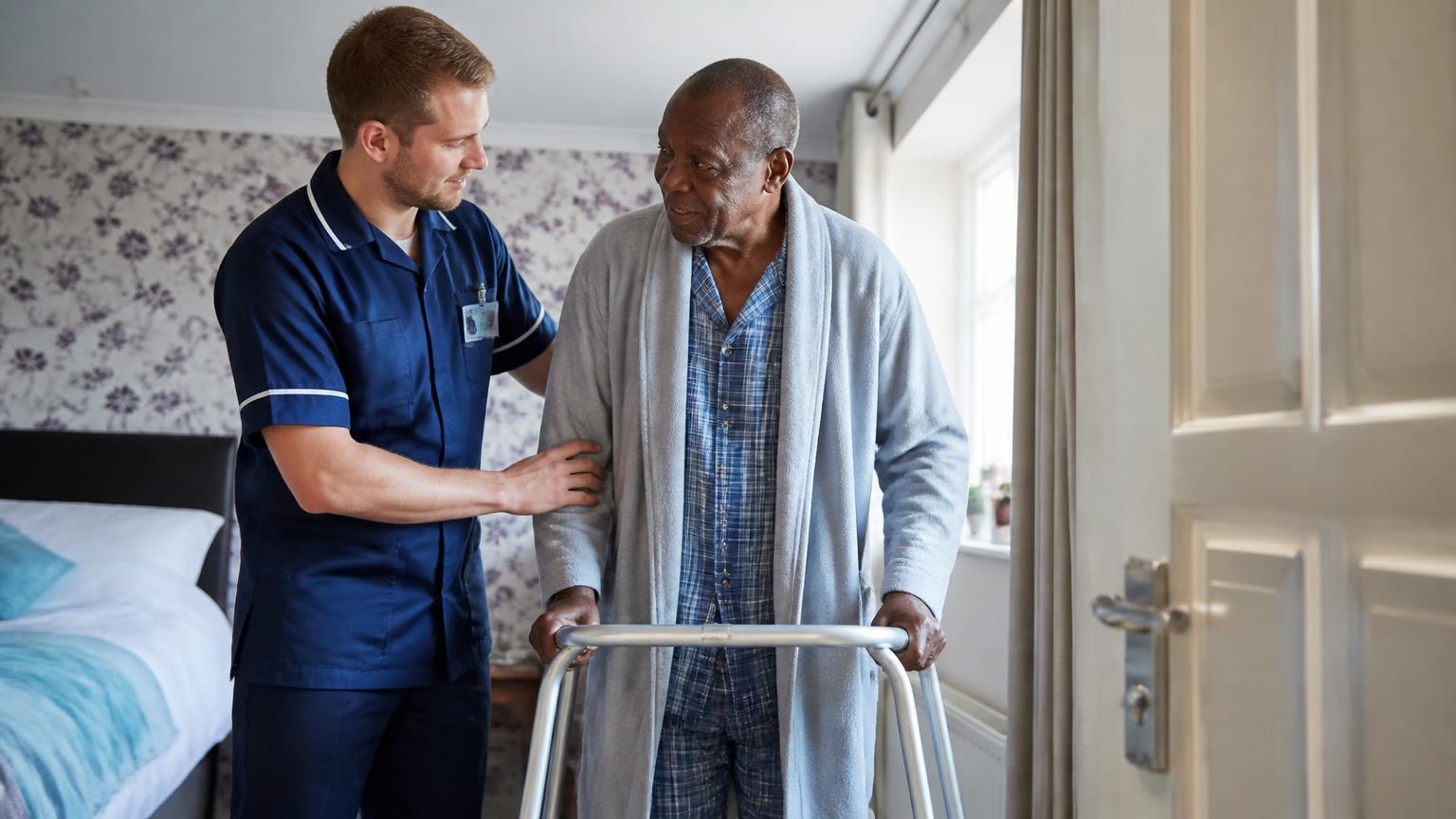 A male carer helping an elderly Black man walk safely at home
